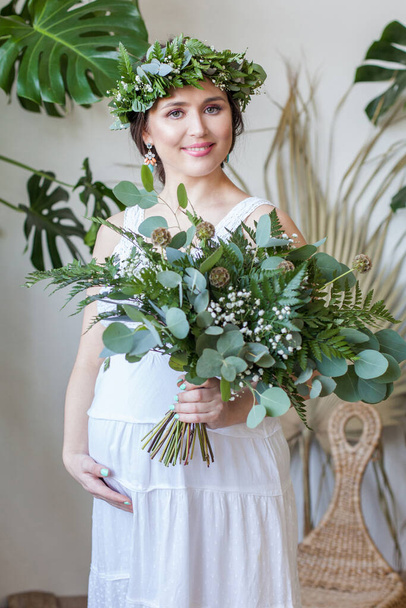 Happy pregnant woman holds flowers bouquet indoor - Photo, Image