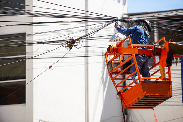 Güvenlik ekipmanı olmayan teknisyen, karmaşık elektrik ve telefon kablolarını tamir etmek ve yönetmek için çalışıyor.. - Fotoğraf, Görsel
