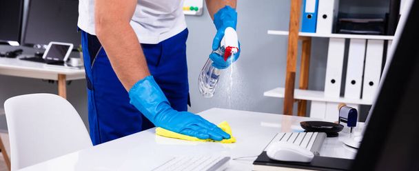 Office Cleaning Service. Janitor Spraying Desk. Workplace Hygiene - Photo, Image