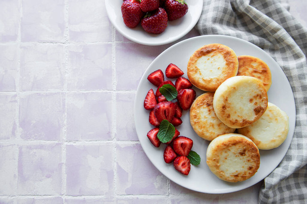 カッテージチーズパンケーキ、新鮮なイチゴとセラミックプレート上のリコッタフリッター。健康的でおいしい朝の朝食。灰色のコンクリートの背景. - 写真・画像
