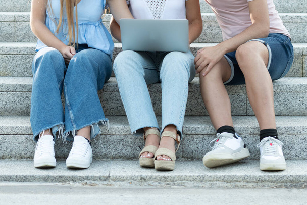 Gesichtslose Studenten sitzen auf einer Treppe und arbeiten an einem Laptop. Teamarbeit im Adoleszenzkonzept. - Foto, Bild