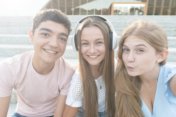 Teenagermädchen macht eine Kuss-Geste und macht ein Selfie mit ihren lächelnden Freunden, die auf der Treppe sitzen. - Foto, Bild