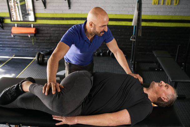 Male personal trainer and physiotherapist assisting mature elderly retired man in stretching. Exercise and assisted strength and injury recovery training for senior man - Foto, immagini