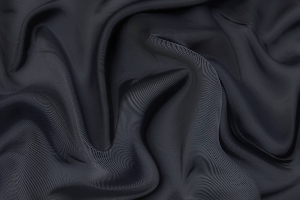 Schwarzer Stoff Textur Hintergrund, welliges Gewebe rutschige schwarze Farbe, Luxus-Satin oder Seide oder Wolle Textur. - Foto, Bild