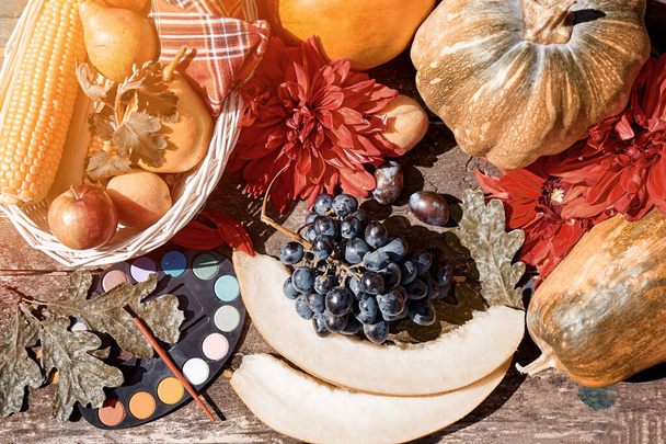 Autumn aesthetic fair: yellow fruits and vegetables and bright paints with a brush, pumpkin, pears, apple and melon. Thanksgiving Day concept. Autumn still life with red georgine, modern shadows. High quality photo - Photo, Image