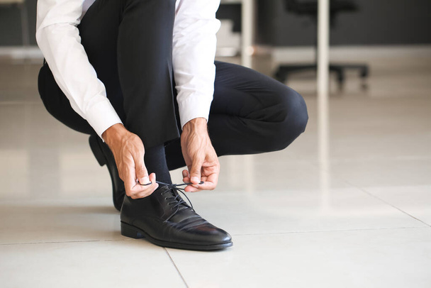 Бізнесмен зав'язує шнурки взуття в офісі
 - Фото, зображення