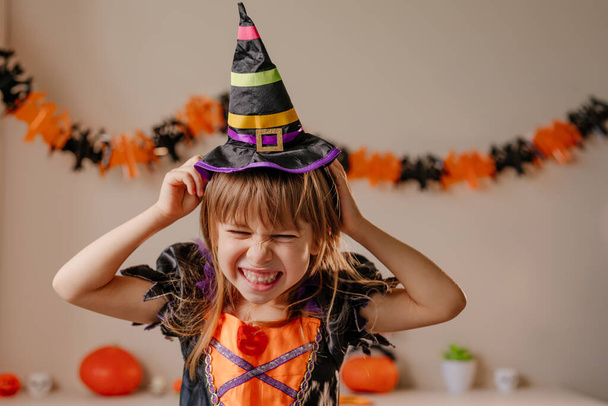 Retrato de niña vestida disfraz de bruja de Halloween y sombrero en la habitación decorada. Enfoque selectivo en la cara. - Foto, imagen