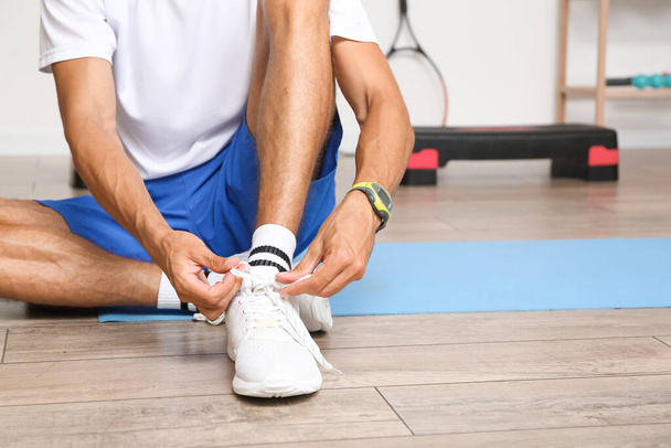 Sporty young man tying shoe laces in gym - Photo, Image