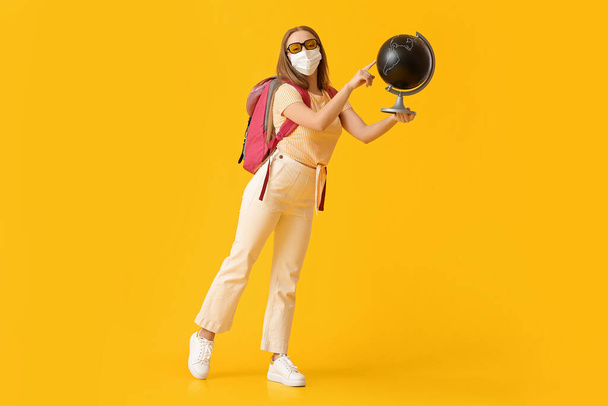 Female tourist in medical mask and with globe on color background - Foto, Bild