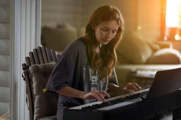 A young woman playing the piano.Close-up of a beautiful blonde girl with reddish-brown hair playing the piano creative, performance, musical concept, she wearing a T-shirt and playing a black piano. - Fotó, kép