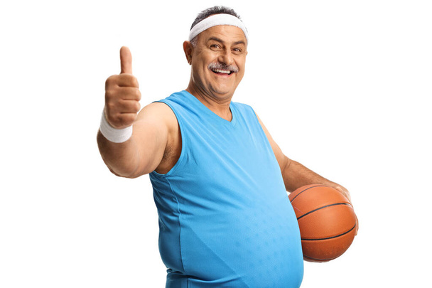 Cheerful mature man gesturing thumbs up and holding a basketball isolated on white background - Photo, Image