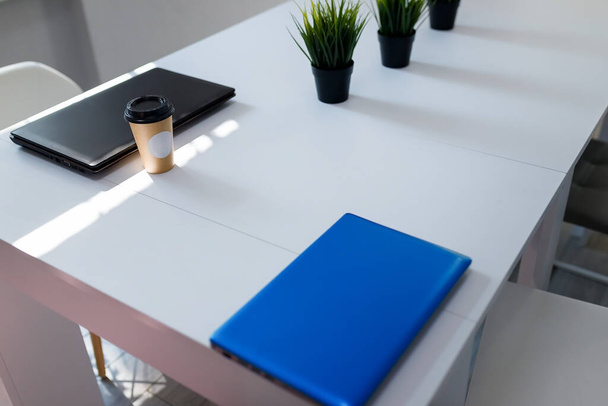 Tazza di caffè usa e getta di carta con etichetta bianca modellata in piedi sul tavolo e due computer portatili. Pausa caffè sul posto di lavoro. - Foto, immagini