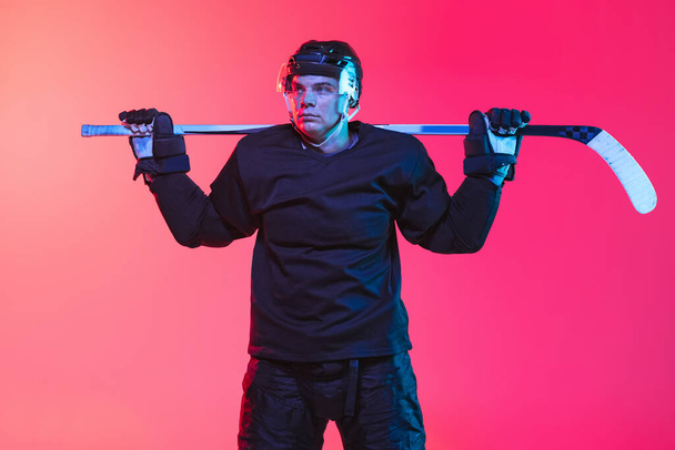 Motivated sportsman. Cropped image of professional hockey playing in uniform with stick isolated over gradient pink background in neon Concept of active life, team game, energy, sport, ad - Foto, Bild