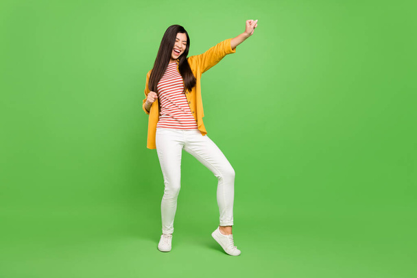 Full length photo of joyful brown hairdo young lady hands fists wear yellow shirt trousers isolated on green color background - Fotó, kép