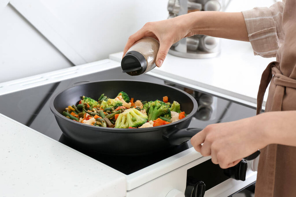 Woman frying vegetables on stove in kitchen, closeup - Foto, afbeelding