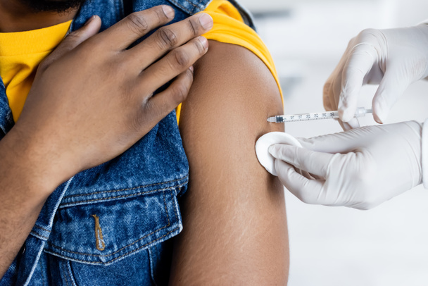 vista recortada de doctor en guantes de látex vacunando hombre afroamericano en clínica - Foto, Imagen