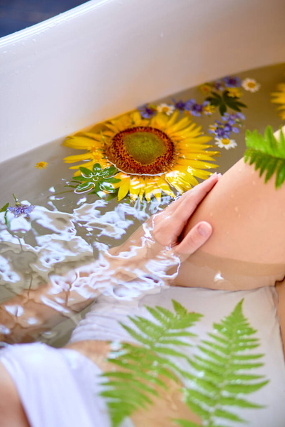 Unrecognizable Woman relaxing in bath with flowers and greenery, organic skin care concept - Фото, зображення