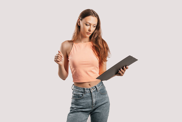 Girl student writes information. Beautiful young business woman isolated on gray background. Achieving career wealth business concept. Mockup copy space. Hold a clipboard with documents - Fotografie, Obrázek