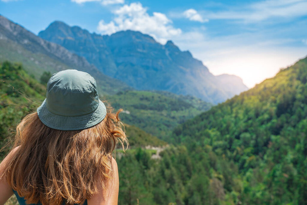 Young woman standing alone outdoors with wild forest mountains in background. Traveling lifestyle and survival concept rear view. Trekking with a green hat. - Foto, Imagem