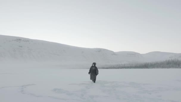 Een man met een beschermend masker tegen wind en vorst wandelt over een sneeuwveld tegen de achtergrond van bergketens - Video