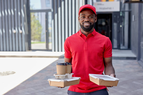 black african young Courier in red uniform delivering fresh food to clients - Zdjęcie, obraz