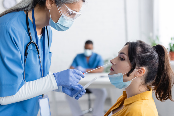 maturo asiatico medico in medico maschera prendere campioni per pcr test da giovane donna in ospedale - Foto, immagini