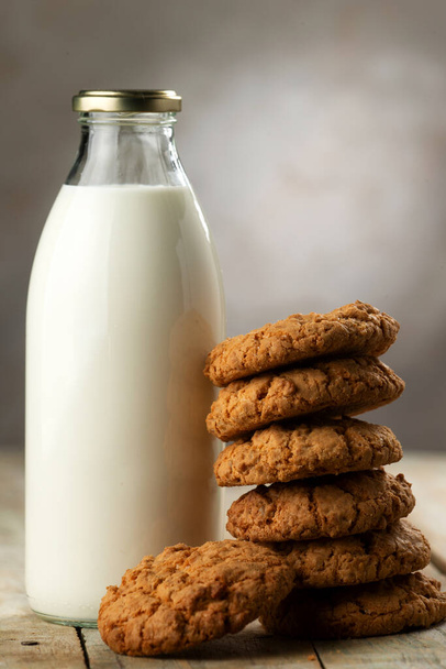 Una bottiglia di latte e una pila di biscotti su un tavolo di legno. Concentrazione selettiva. Primo piano - Foto, immagini