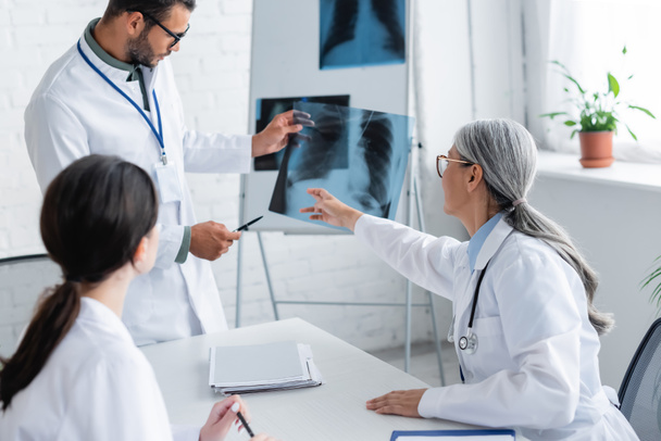 mature asian doctor pointing at lungs x-ray during meeting with young colleagues - Photo, Image