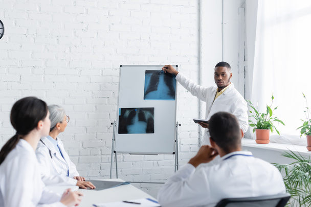 Африканский американский врач указывает на рентген легких вблизи размытых коллег во время совета - Фото, изображение