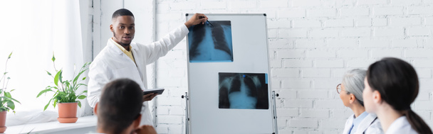 médecin afro-américain pointant vers les poumons rayons X sur flip chart pendant le conseil avec des collègues flous, bannière - Photo, image
