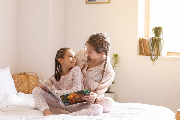 Κοριτσάκι με τη μητέρα της να διαβάζει παραμύθια στην κρεβατοκάμαρα. - Φωτογραφία, εικόνα