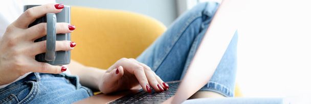 Vrouwelijke handen op laptop toetsenbord met beker - Foto, afbeelding