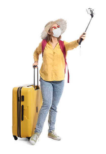 Turista femenina en máscara médica tomando selfie sobre fondo blanco - Foto, Imagen