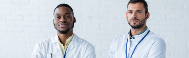 african american and european doctors in white coats looking at camera, banner - Foto, immagini