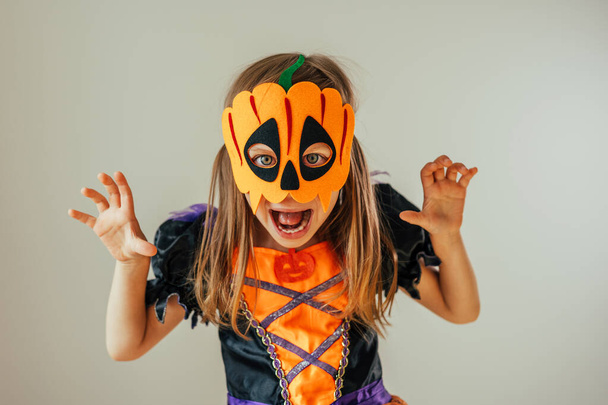 Πορτρέτο του μικρού κοριτσιού ντυμένος Απόκριες κοστούμι μάγισσα και κολοκύθα μάσκα εσωτερικού χώρου. Επιλεκτική εστίαση. - Φωτογραφία, εικόνα