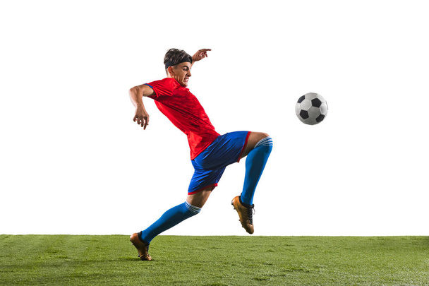 Photo in motion of young soccer football player kicking ball with knee in a jump. Man training in uniform isolated over white background. Concept of action, team sport game, energy. Copy space for ad - Photo, Image