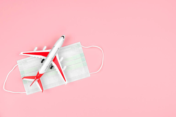 An overhead view of a red and white toy plane and a protective medical mask on a pink background. Safe travel concept. Traveling during a pandemic - Photo, Image