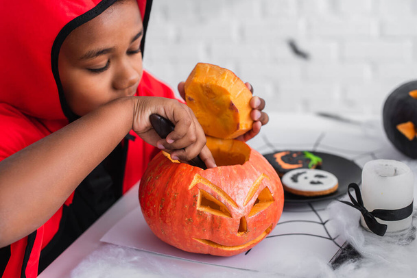 african american boy in halloween costume carving pumpkin  - Fotó, kép