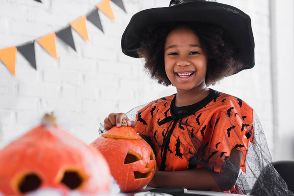 feliz africano americano chica en bruja halloween traje cerca caved calabazas   - Foto, imagen
