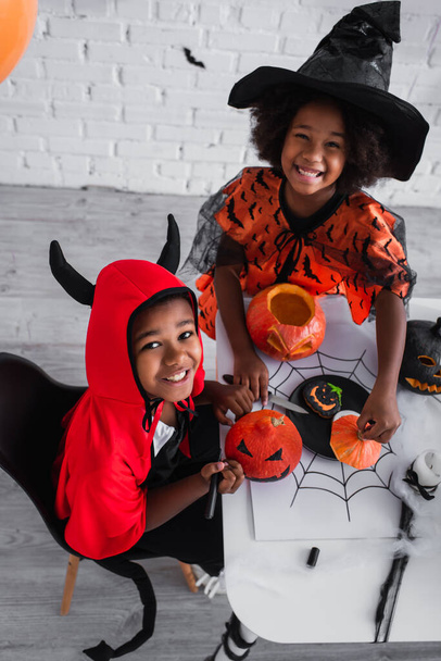 high angle view of happy african american children in halloween costume decorating pumpkins  - Photo, Image