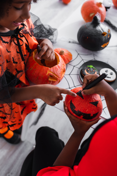 happy african american girl pointing at drawing on pumpkin near brother  - Photo, Image