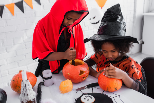 african american children in halloween costumes carving pumpkins  - 写真・画像