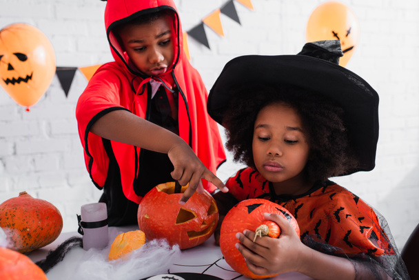 african american boy pointing at carved pumpkin near sister in witch costume  - Photo, Image