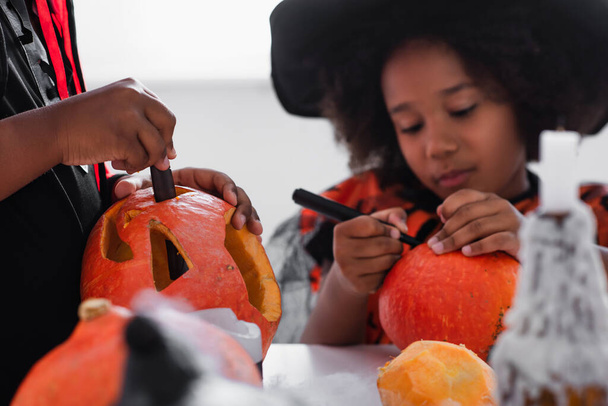 african american boy carving pumpkin while sister drawing on blurred background  - Foto, imagen