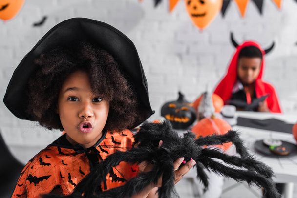 kísérteties afro-amerikai lány boszorkány jelmezben tartja játék pók közelében elmosódott testvér - Fotó, kép