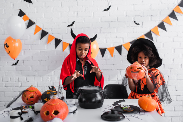 enfants afro-américains en costumes d'Halloween préparant potion au chaudron de sorcière - Photo, image