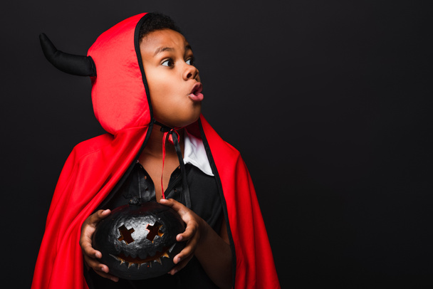 spettrale africano americano bambino tenendo intagliato zucca scura isolato su nero - Foto, immagini