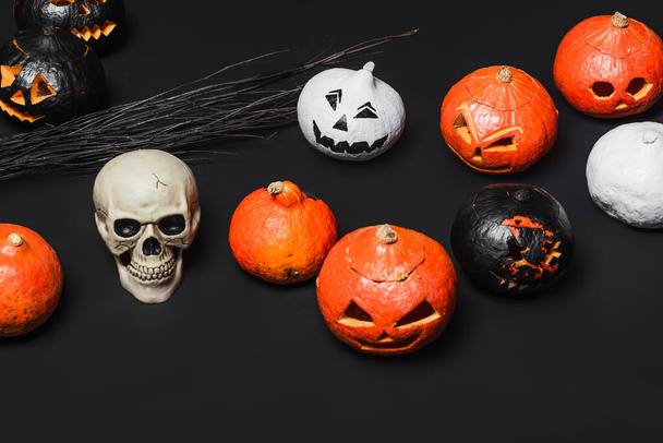 skull near broom and carved pumpkins on black  - Foto, afbeelding