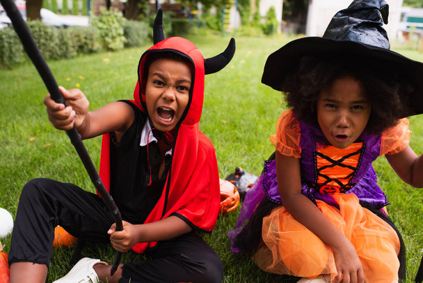 african american siblings in halloween costumes screaming while playing on backyard - Foto, imagen