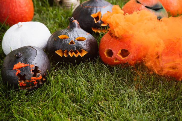 orange smoke near carved and spooky pumpkins on green lawn - Foto, afbeelding